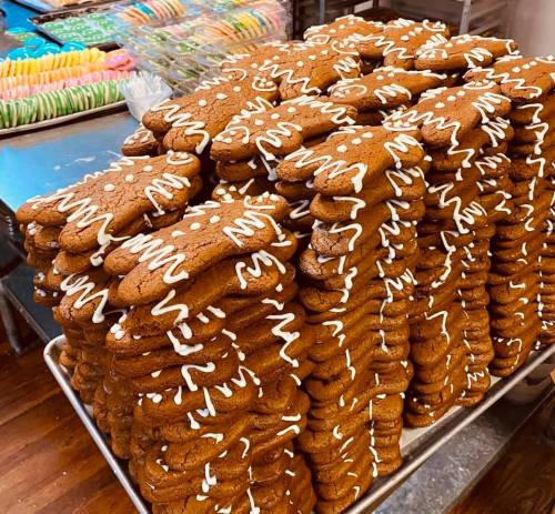 A large stack of gingerbread cookies decorated with white icing, set on a baking tray in a bakery.