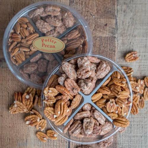 A clear container with divided sections holds various pecans, some coated and some plain, on a wooden surface.