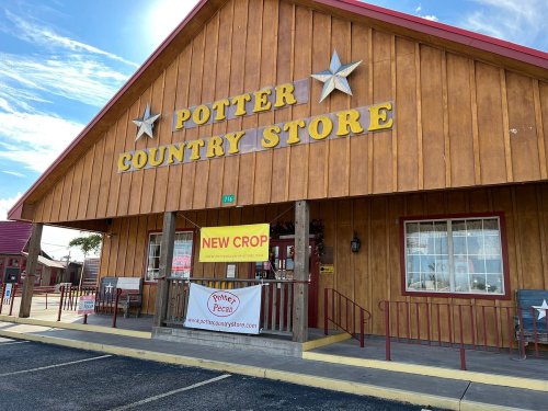 Exterior of Potter Country Store with wooden siding, large yellow sign, and a banner reading "NEW CROP." Clear blue sky.