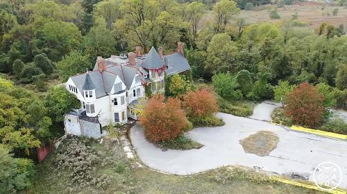Aerial view of an abandoned mansion surrounded by overgrown trees and autumn foliage.