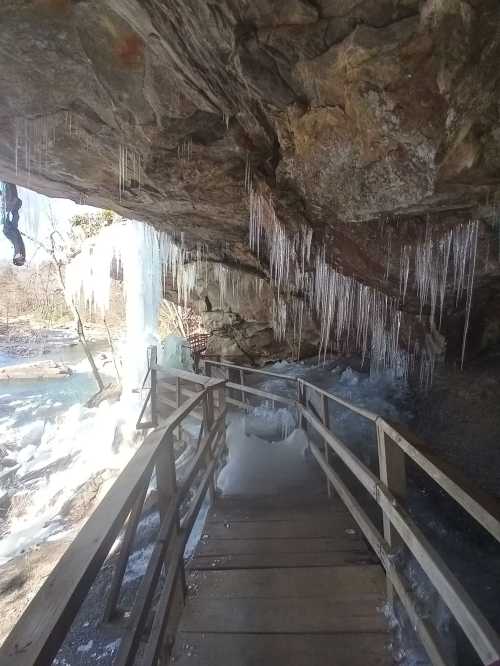 A wooden walkway leads through a cave with icicles hanging from the ceiling and ice on the ground.