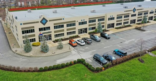 Aerial view of a commercial building with parked cars and landscaped greenery in the foreground.