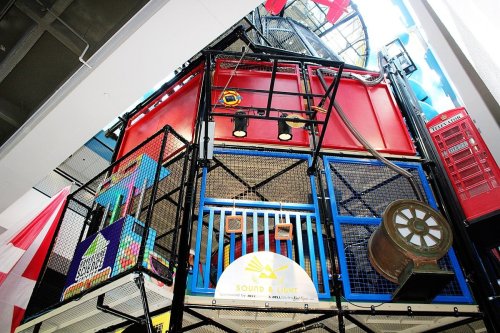 Colorful indoor play structure with climbing nets, slides, and various interactive elements in a bright, spacious environment.