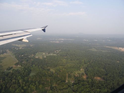 View from an airplane wing, showcasing green landscapes and distant hills under a clear sky.