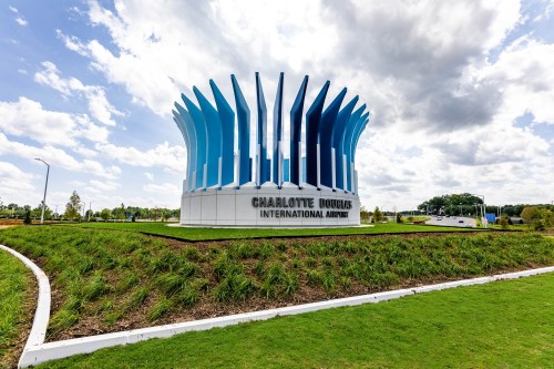 Sign for Charlotte Douglas International Airport, featuring a modern design with blue accents against a cloudy sky.
