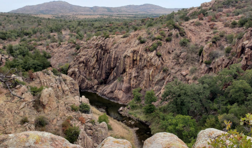 A scenic view of rocky cliffs and a winding river surrounded by lush greenery and rolling hills.