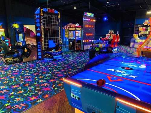 A vibrant arcade filled with various games, colorful carpet, and bright lights, featuring air hockey and ticket machines.