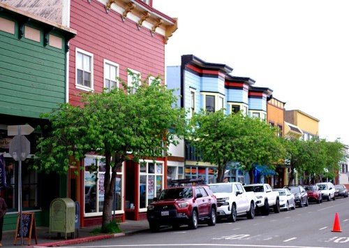 Colorful buildings line a street, with trees and parked cars, creating a vibrant urban scene.
