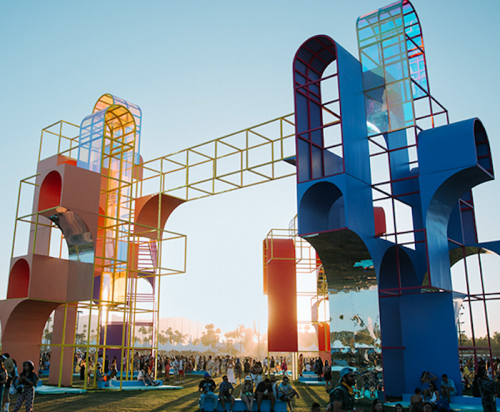 Colorful geometric structures with people gathered below, set against a bright sky during a festival.