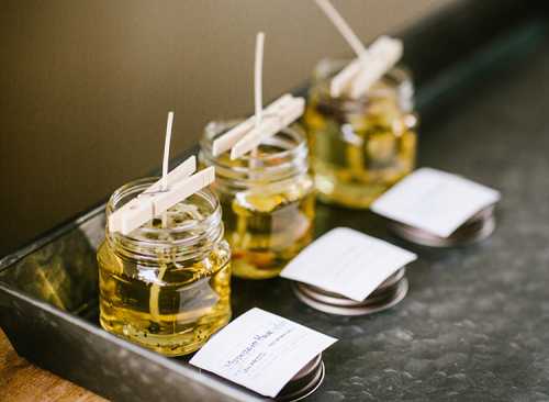 Three jars of candle wax with wooden wicks and labels, arranged on a dark tray.