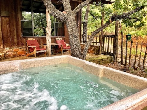 A hot tub with bubbling water, surrounded by trees and a rustic cabin in a serene outdoor setting.