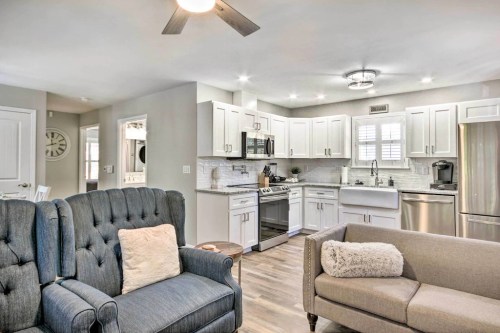 A modern kitchen with white cabinets, stainless steel appliances, and a cozy living area featuring a blue armchair and gray sofa.