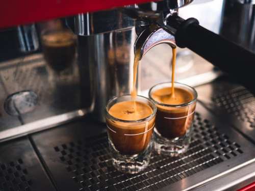 Two espresso shots are being brewed into small glass cups from a coffee machine.