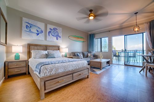 Cozy bedroom with a wooden bed, ocean-themed decor, and large windows overlooking a balcony with a sea view.