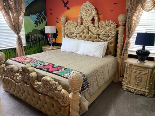 Luxurious bedroom featuring an ornate gold bed, colorful wall mural, and elegant curtains with matching nightstands.