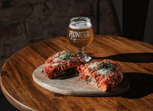 A wooden table with two slices of pizza topped with sauce and cheese, alongside a glass of beer.