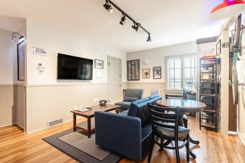Cozy living room with a blue sofa, wooden table, TV, and wall decor, featuring natural light from a window.