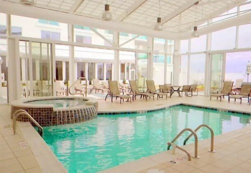 Indoor pool area featuring a hot tub, lounge chairs, and large windows letting in natural light.