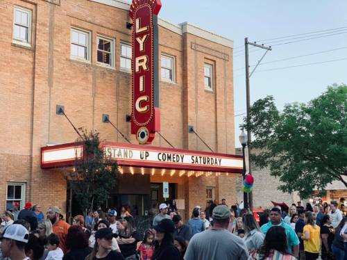 Crowd gathered outside the Lyric Theater for a stand-up comedy event, with a marquee sign and trees in the background.