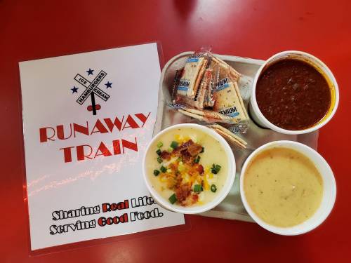 A tray with three bowls of soup and crackers, next to a sign that reads "Runaway Train" with a slogan about good food.
