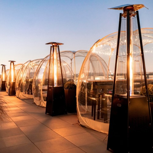 A rooftop terrace with transparent domes and outdoor heaters, set against a twilight sky.