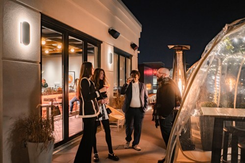 Four people chatting on a rooftop at night, with warm lighting and a cozy atmosphere.