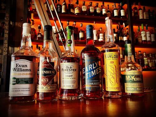 A selection of bourbon whiskey bottles displayed on a bar shelf with a warm, illuminated background.