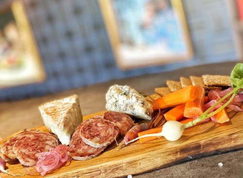 A wooden platter featuring assorted meats, cheeses, crackers, and fresh vegetables, beautifully arranged.