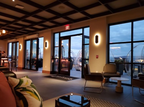 A modern lounge area with large windows, showcasing a view of outdoor pods and a cloudy evening sky.