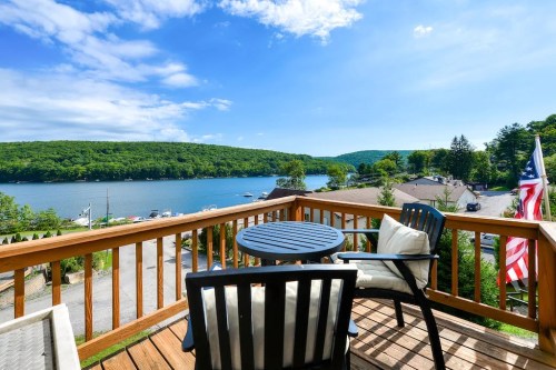 A scenic view from a deck overlooking a lake surrounded by green hills and blue skies.