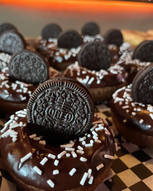 Close-up of chocolate donuts topped with Oreo cookies and white sprinkles on a checkered surface.