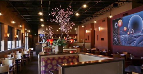 Interior of a restaurant featuring a mural, decorative plants, and a cozy dining area with wooden tables and chairs.