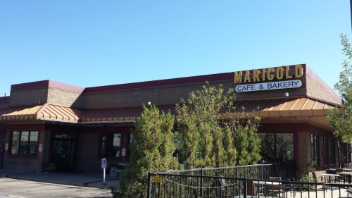Exterior of Marigold Cafe & Bakery, featuring a sign and greenery under a clear blue sky.