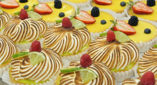 A display of beautifully decorated desserts with meringue, fruit toppings, and vibrant colors.