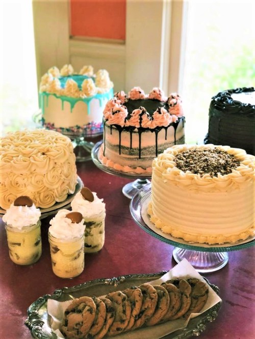 A variety of decorated cakes and desserts displayed on a table, including cookies and parfaits in glass cups.