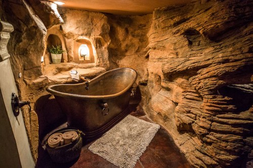 A rustic bathroom featuring a copper bathtub surrounded by natural stone walls and soft lighting.