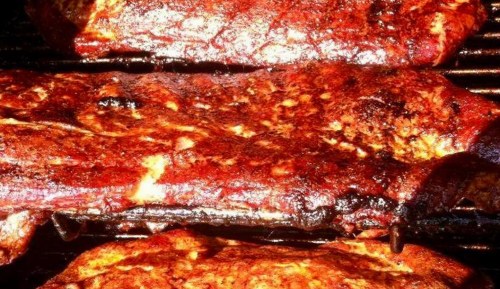 Close-up of three pieces of grilled meat with a smoky, charred surface and a rich, reddish-brown seasoning.