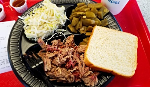 A plate with pulled pork, coleslaw, green beans, a slice of bread, and a drink on a red tray.