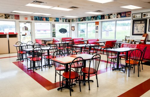 A diner interior with red and black chairs, tables, and walls decorated with vintage music posters.