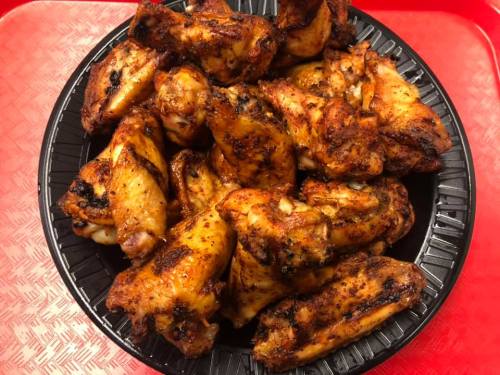 A platter of golden-brown, seasoned chicken wings arranged neatly on a black tray.