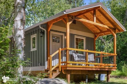 A small, modern cabin with a wooden porch, surrounded by trees and greenery.