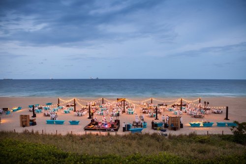 A beautifully arranged beach event with tables, lights, and decorations set against a serene ocean backdrop.