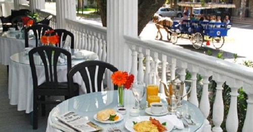 A charming outdoor dining setup with tables, flowers, and a breakfast spread, featuring a horse-drawn carriage in the background.