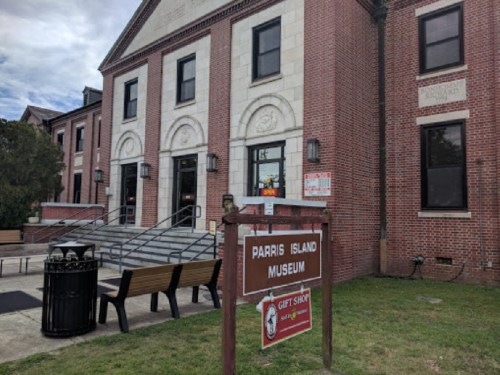 Exterior of the Parris Island Museum, featuring brick architecture, a sign, and benches in front.