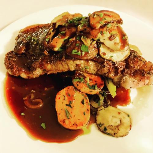 A juicy steak topped with sautéed mushrooms and carrots, served on a plate with a rich sauce and garnished with herbs.