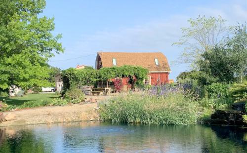 A red barn surrounded by greenery and flowers, reflecting in a calm pond under a clear blue sky.