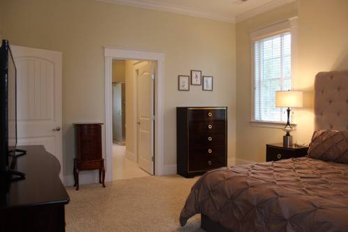 A cozy bedroom featuring a bed, dresser, lamp, and an open door leading to a bathroom. Soft lighting and neutral colors.