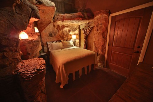 Cozy cave-like bedroom with a bed, warm lighting, and stone walls, creating a rustic and inviting atmosphere.