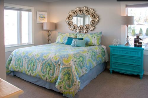 A cozy bedroom featuring a large bed with a colorful paisley quilt, a turquoise nightstand, and decorative lamps.