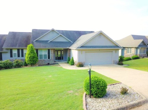 A single-story house with a stone facade, green lawn, and a driveway, surrounded by well-maintained landscaping.